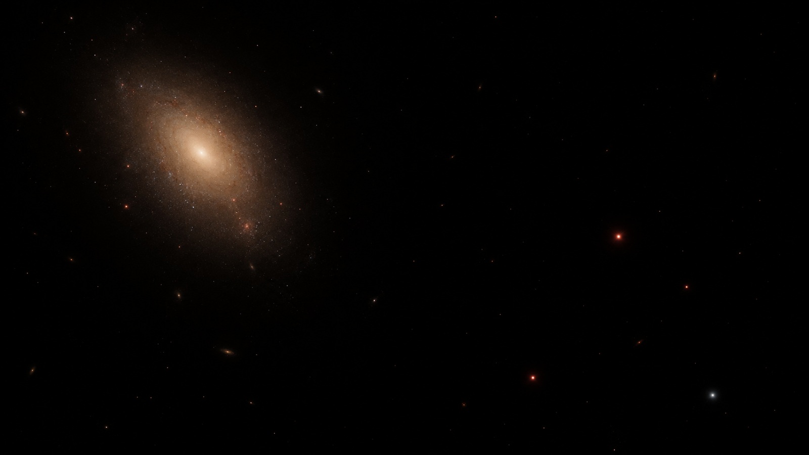 Artist's possible far-future scene with a dim amber elliptical galaxy and sparse cool stellar points surrounded by dark space.